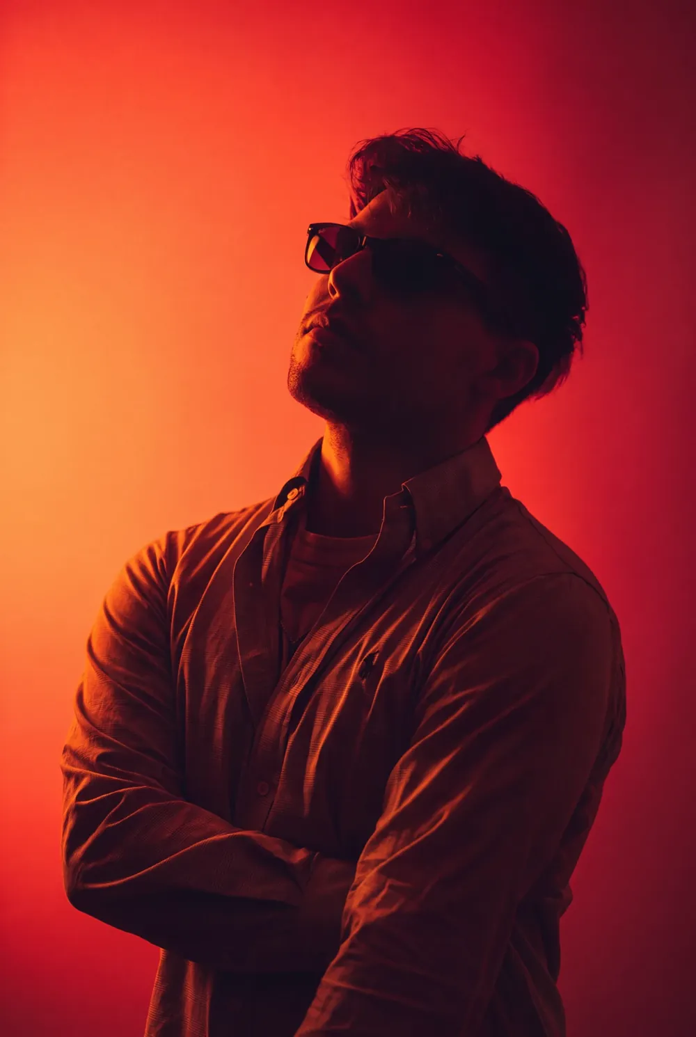 Portrait of Samuele Napolano in semi-silhouette, wearing sunglasses and looking up, against an orange-to-red backdrop